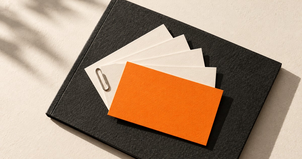 An orange business card on cream cards and a dark folio.
